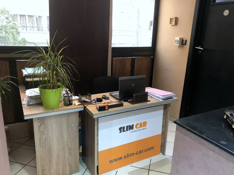 Le bureau d'accueil de l'agence Slim Car, avec son panneau « Slim Car – Location de voiture »
